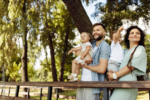 Happy family with little kids at the park, beautiful mother hold in arms joyful son, adorable daughter in caring fathers arms smiling, parenting and childhood concept