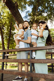 Lovely parents with little kids at the park, beautiful mother hold in arms joyful son, cute daughter sitting in fathers hands, enjoy happy family moments, weekend outdoors concept