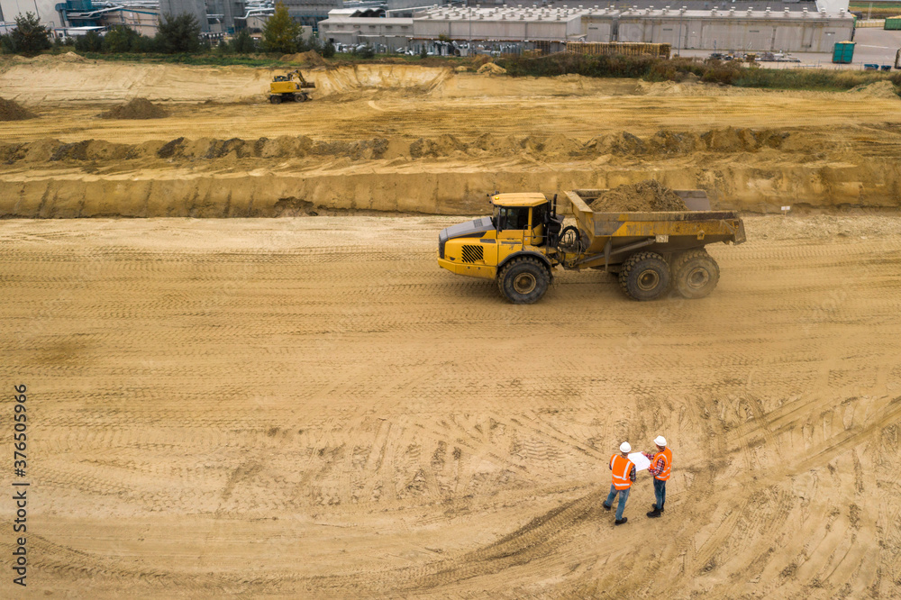 Obraz premium Top view of two road construction workers in orange vests and protective helmets in the middle on the field