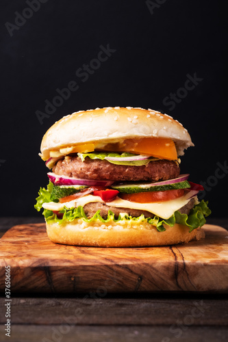 Classical burger with tomatos, beef, cheddar, salat, fresh cucumber and ketchup on wooden background with copy space, isometric vertical orientation