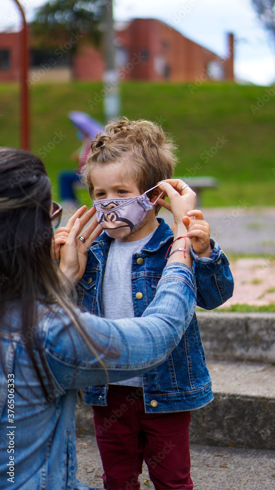 Obraz premium Caucasian mother putting face mask on her son in the park, Back to School 