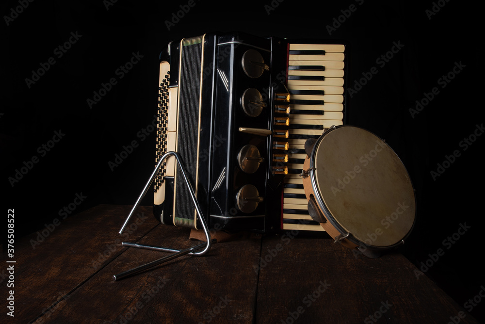 Old accordion, tambourine and triangle on rustic wooden surface with black background and Low