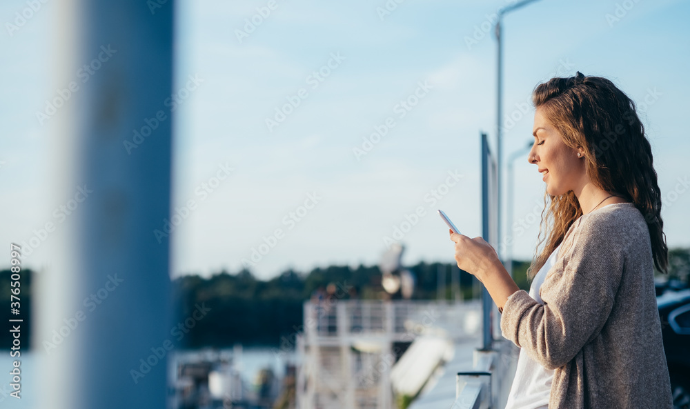Cheerful woman using phone next to river outside
