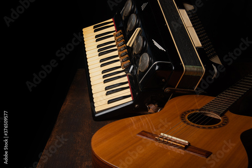 Old accordion and a beautiful guitar composing a scene on a rustic wooden surface with black background and low key lighting, selective focus.