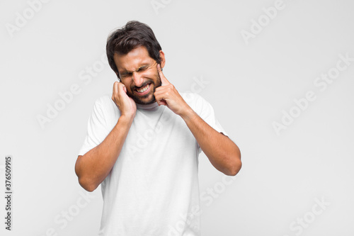 Фотография young latin handsome man looking angry, stressed and annoyed, covering both ears