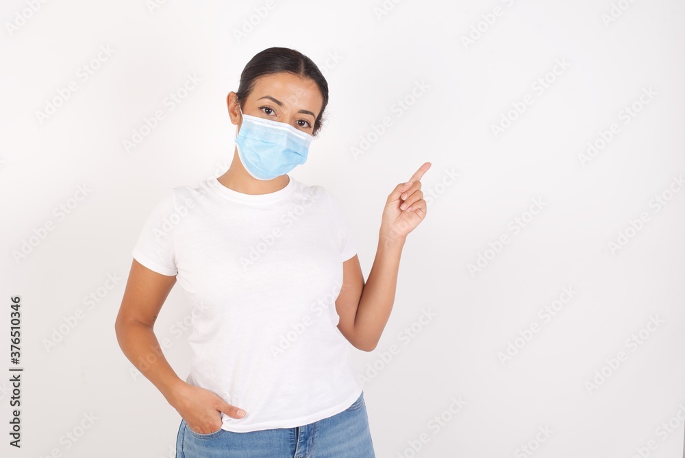 Young arab woman wearing medical mask standing over isolated white background looking indicating fingers hands side empty space advising novelt Young arab woman wearing medical mask standing over isolated white background looking indicating fingers hands side empty space advising novelt