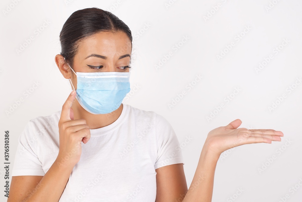 Funny Young arab woman wearing medical mask standing over isolated white background with short hair holding open palm new product. I wanna buy it! Funny Young arab woman wearing medical mask standing over isolated white background with short hair holding open palm new product. I wanna buy it!