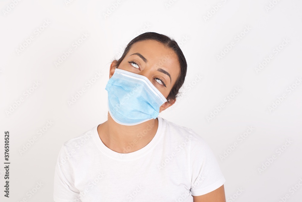 Young arab woman wearing medical mask standing over isolated white background looking sleepy and tired, exhausted for fatigue and hangover, lazy eyes in the morning.