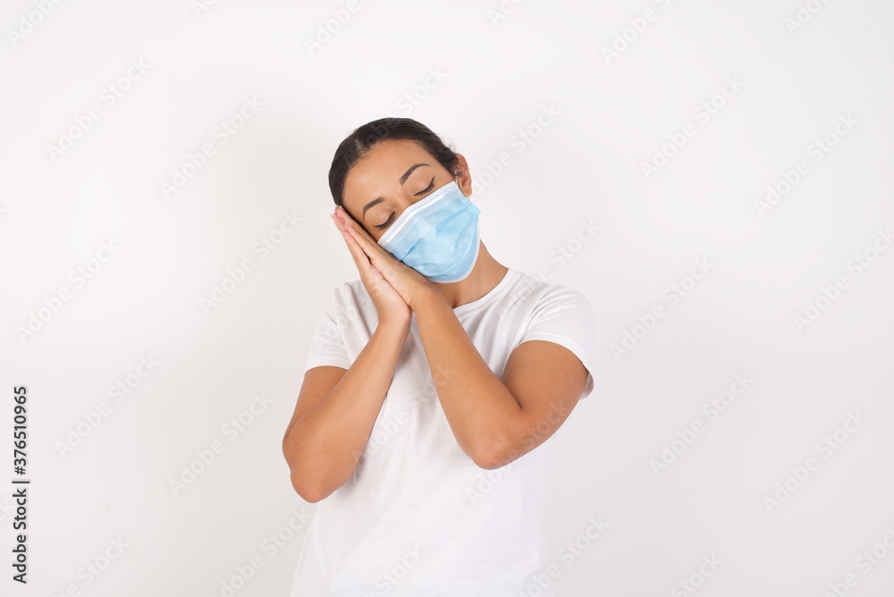 Young arab woman wearing medical mask standing over isolated white background sleeping tired dreaming and posing with hands together while smiling with closed eyes. Young arab woman wearing medical mask standing over isolated white background sleeping tired dreaming and posing with hands together while smiling with closed eyes.