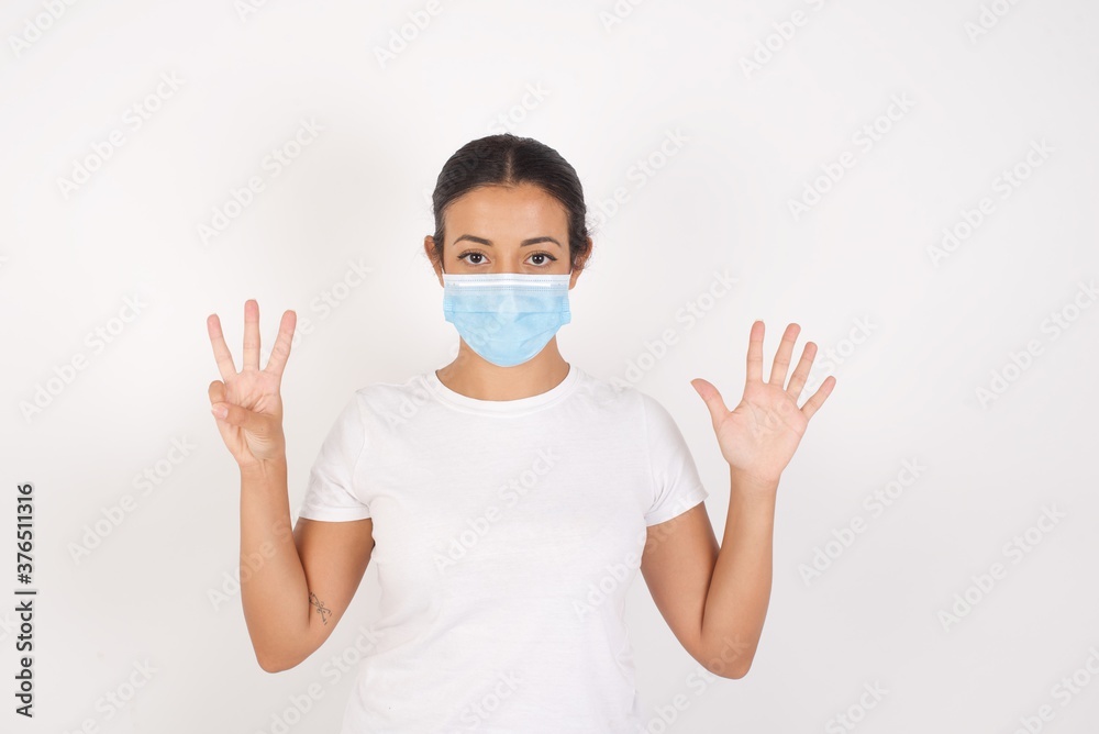 Young arab woman wearing medical mask standing over isolated white background showing and pointing up with fingers number eight while smiling confident and happy. Young arab woman wearing medical mask standing over isolated white background showing and pointing up with fingers number eight while smiling confident and happy.