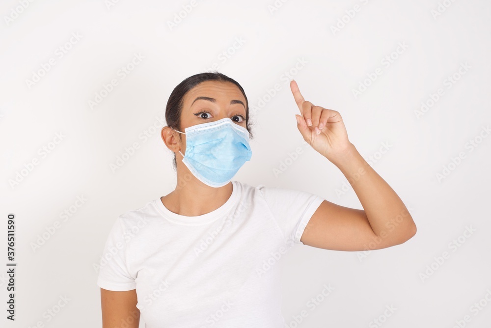 Young arab woman wearing medical mask standing over isolated white background pointing finger up with successful idea. Exited and happy. Number one. Young arab woman wearing medical mask standing over isolated white background pointing finger up with successful idea. Exited and happy. Number one.