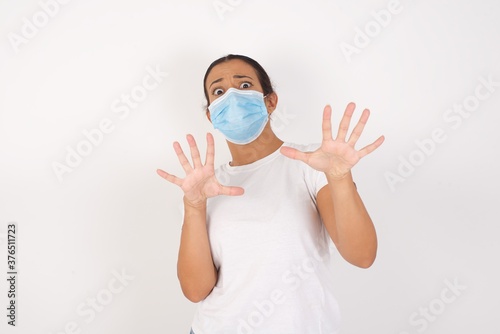 Young arab woman wearing medical mask standing over isolated white background afraid and terrified with fear expression stop gesture with hands, shouting in shock. Panic concept.