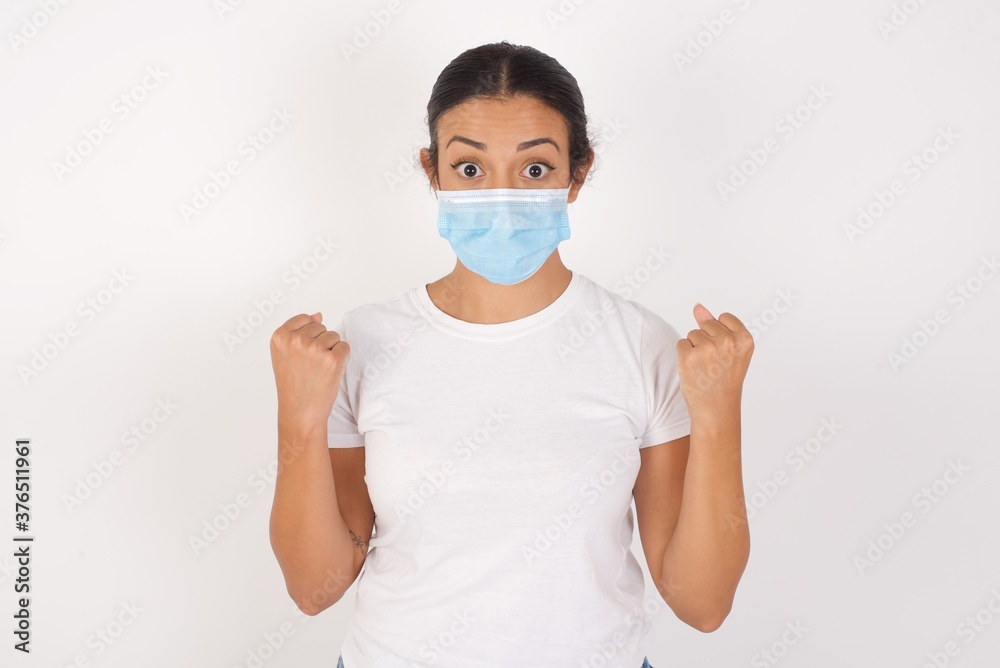 Young arab woman wearing medical mask standing over isolated white background celebrating surprised and amazed for success with arms raised and open eyes. Winner concept. Young arab woman wearing medical mask standing over isolated white background celebrating surprised and amazed for success with arms raised and open eyes. Winner concept.
