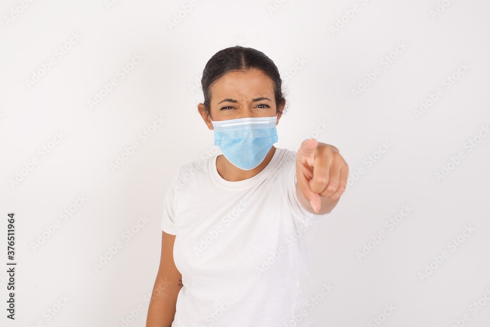 Young arab woman wearing medical mask standing over isolated white background pointing displeased and frustrated to the camera, angry and furious ready to fight with you. Young arab woman wearing medical mask standing over isolated white background pointing displeased and frustrated to the camera, angry and furious ready to fight with you.