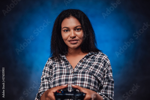 African female player holds in her arms favourite game device in smoke blue backround.