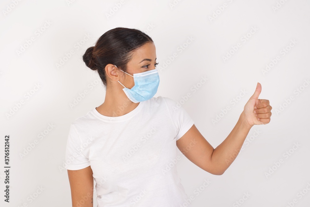 Young arab woman wearing medical mask standing over isolated white background Looking proud, smiling doing thumbs up gesture to the side. Good job! Young arab woman wearing medical mask standing over isolated white background Looking proud, smiling doing thumbs up gesture to the side. Good job!