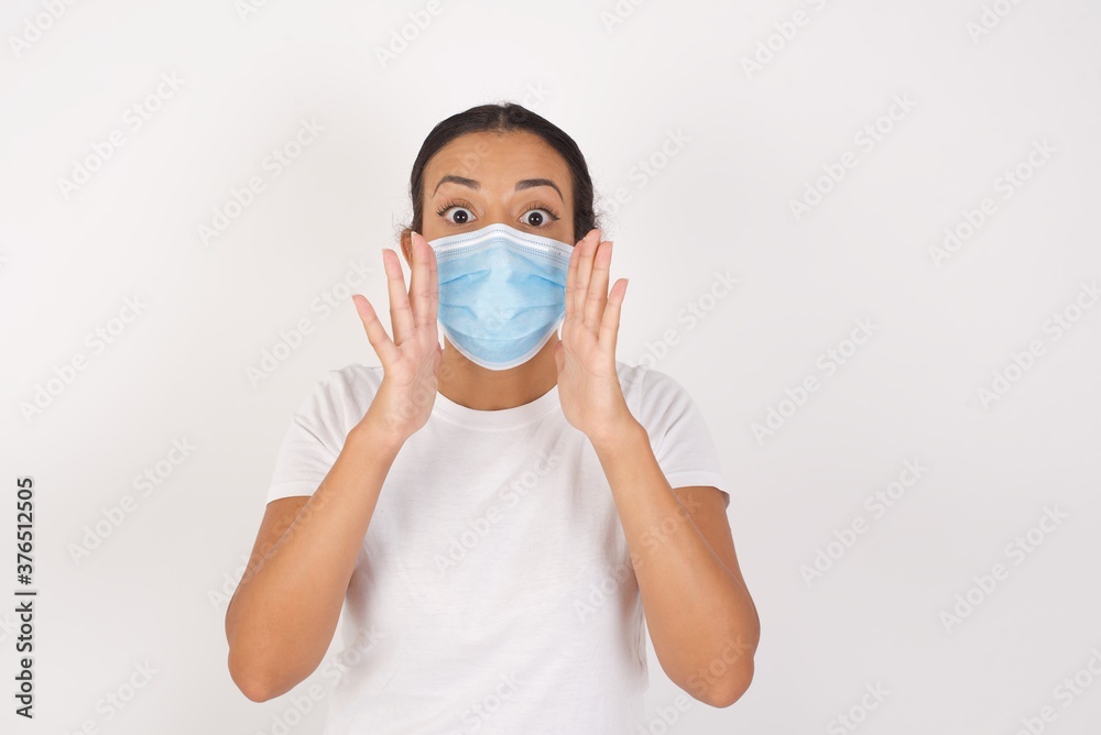 Young arab woman wearing medical mask standing over isolated white background, shouting excited to front. Young arab woman wearing medical mask standing over isolated white background, shouting excited to front.