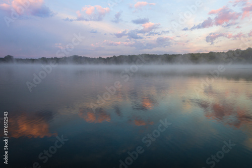 Fog lifts off the lake with dramatic cloudscape at sunrise creating a peaceful relaxing scene with copy space