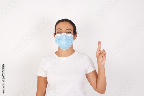 Young arab woman wearing medical mask standing over isolated white background pointing up with fingers number ten in Chinese sign language Shi