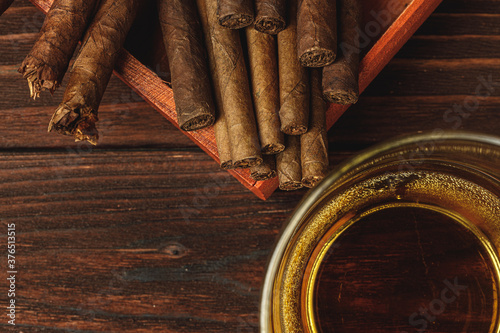 Foto Glass of whiskey and rolled cigars on wooden table