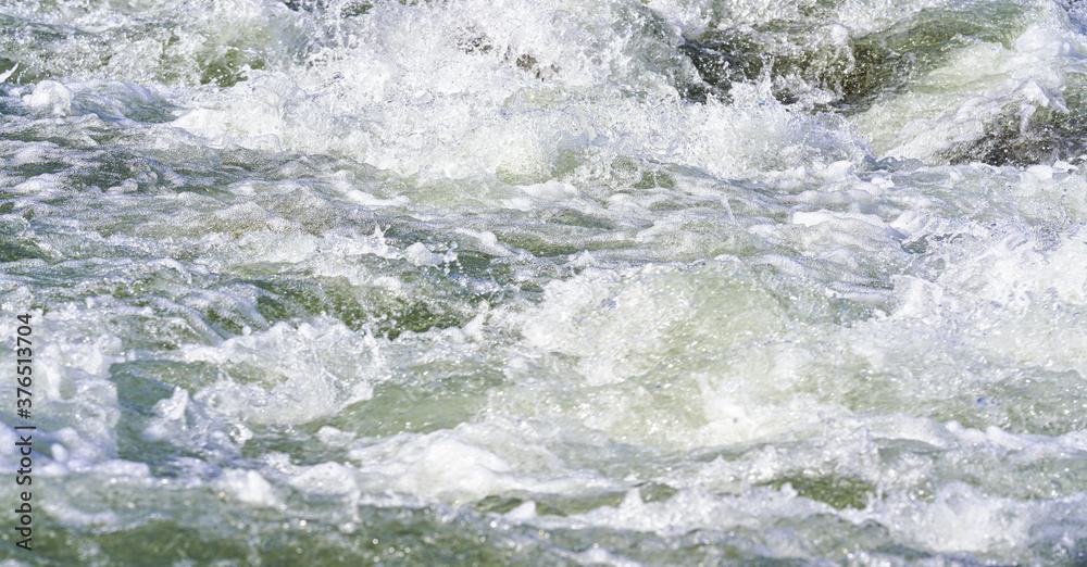 Rapid spring river flowing over rocks on sunny day, forming white water waves, closeup detail - abstract nature background Rapid spring river flowing over rocks on sunny day, forming white water waves, closeup detail - abstract nature background