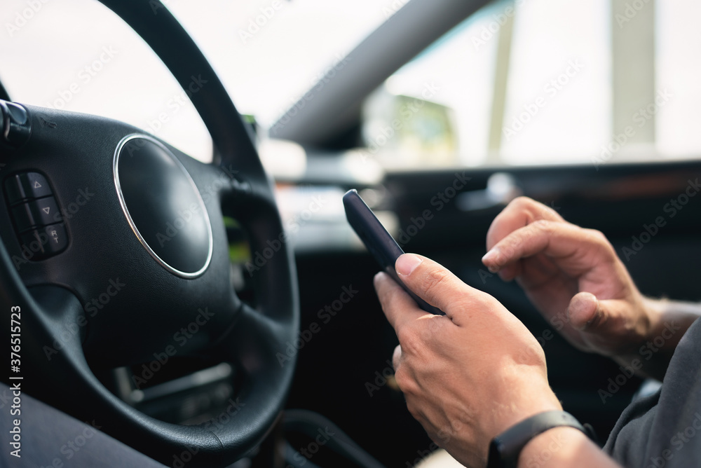 Driver with a mobile phone is sitting by the car steering wheel close up.