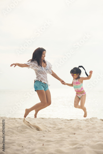 Asian mother with daughter resting on a tropical beach during summer vacations. Asia mother and daughter jumping at the beach