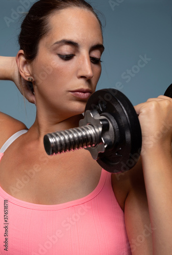 Close up of a young caucasian woman focused on her exercise with a dumbbell isolated on a blue background