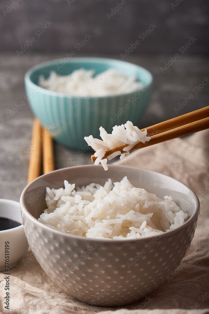Rice chopsticks, over a bowl of white rice, soy sauce on a dark gray background