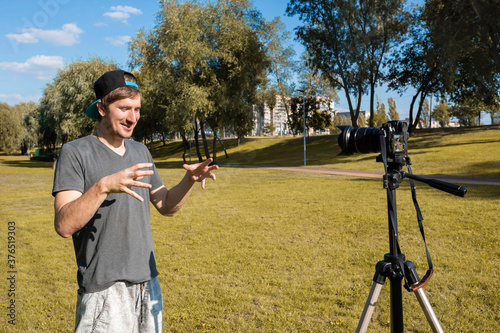 Happy young male speaker in front of the camera, recording training videos, outdoors on a sunny day.
