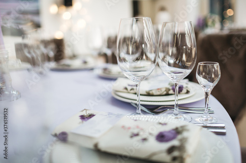 Wine glasses on the decorated table for the wedding celebration, cutlery and plates for the birthday party, restaurant table serving in white and violet colors, front view, peopleless