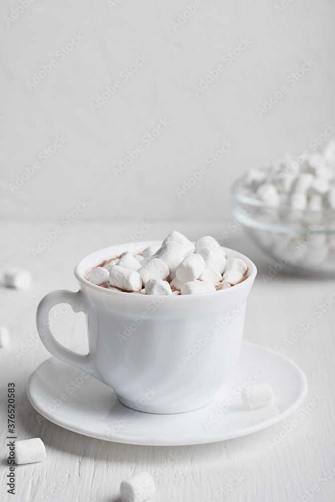 White cup full of warm sweet homemade cacao drink usually prepared at cold winter and autumn sesons served on plate with bowl of marshmallows on wooden background. Vertical orientation image White cup full of warm sweet homemade cacao drink usually prepared at cold winter and autumn sesons served on plate with bowl of marshmallows on wooden background. Vertical orientation image