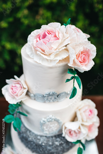 Close up of beautiful tender wedding cake decorated with dim pink roses. Traditional symbol of wedding celebration. Complicated recipe of sweet baked confectionery. 