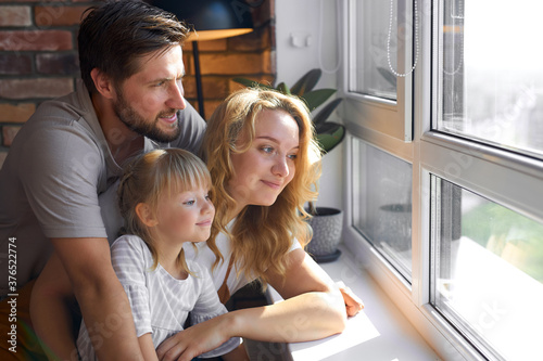 happy young family looking through the window at home, look at the street, happy together.