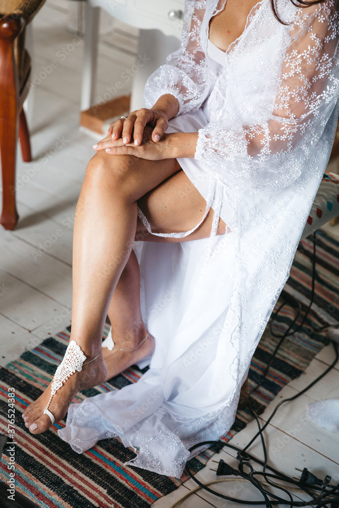 Crop view of beautiful barefoot legs with tan and fashionable foot bracelet. Young bride with perfect body, dressing up, morning before wedding ceremony. Concept of bridal preparing and getting ready.