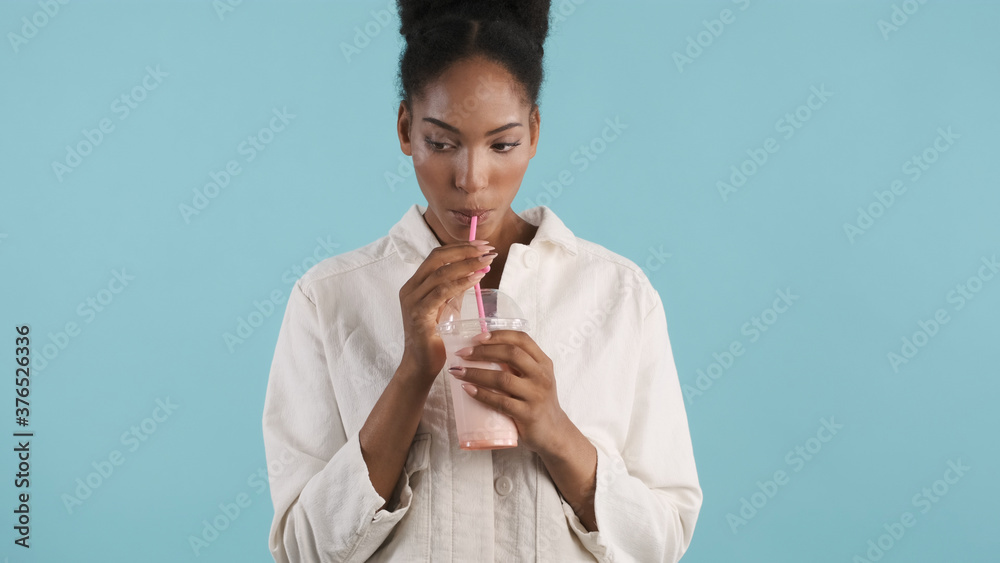 Pretty casual african american girl drinking delicious milkshake on camera over colorful background Pretty casual african american girl drinking delicious milkshake on camera over colorful background