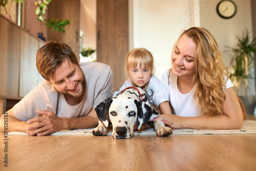 portrait of young caucasian family having fun with dog at home, parents and child rest, relax at home, take care of dalmatian dog