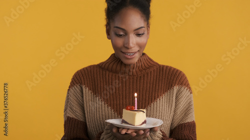 Beautiful cute african american girl with slice of birthday cake making a wish over colorful background