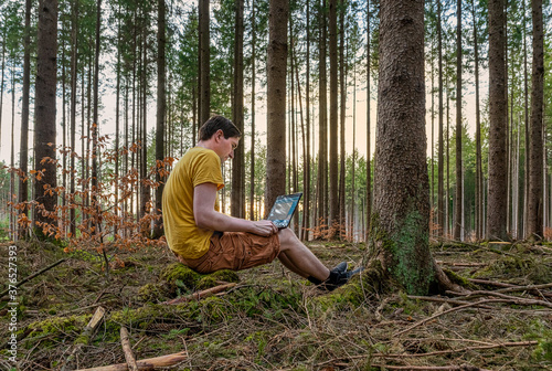 A man working outdoor with his laptop in a forest on the fresh air, home office in the green forest in front of your home.