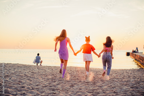 Three young girl running along the sandy beach into the sea. Back view. Rest on the sea, sunbathing, healthy lifestyle.