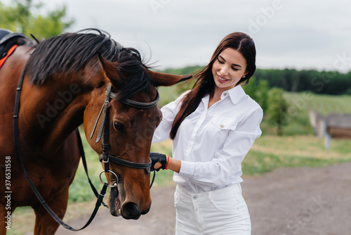 A young pretty girl rider poses near a thoroughbred stallion on a ranch. Horse riding, horse racing