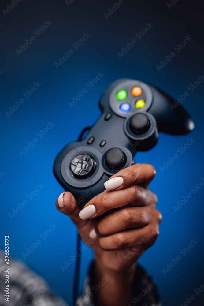 Groomed and pretty afro woman's hand is holding a joystick and pointing it up in foggy blue background. Feminine gaming. Groomed and pretty afro woman's hand is holding a joystick and pointing it up in foggy blue background. Feminine gaming.
