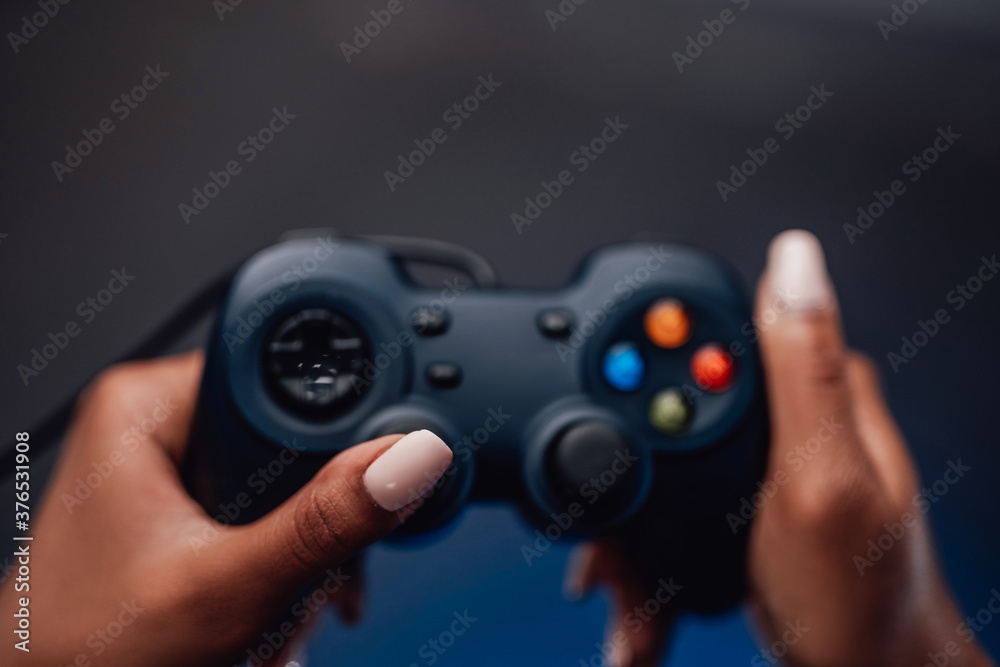 Modern gaming entertainment and sport field. Feminine blackskinned hands holds gaming device in smoke blue background. Modern gaming entertainment and sport field. Feminine blackskinned hands holds gaming device in smoke blue background.