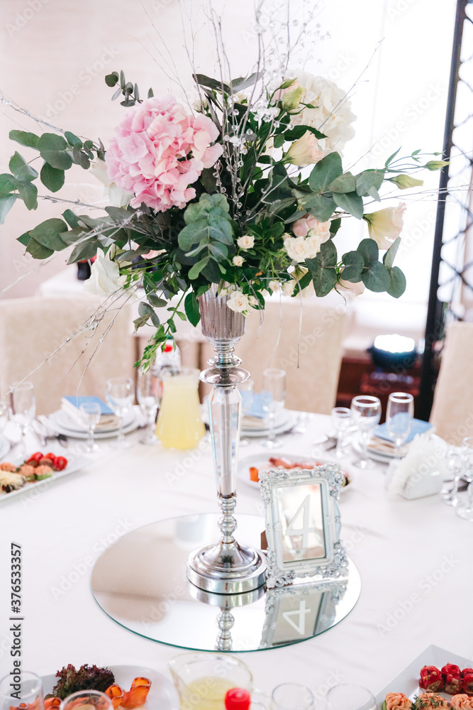 Front view of vase with floral composition made of eucalyptus and pale pink flower. Wedding table serving. Beautiful florist job. Restaurant adornment for birthday celebration. Concept of atmosphere.