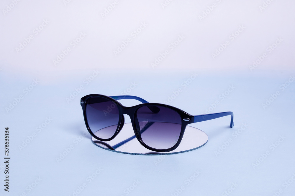 sunglasses with an iridescent degrade crystal above a mirror on a blue background that fades to white