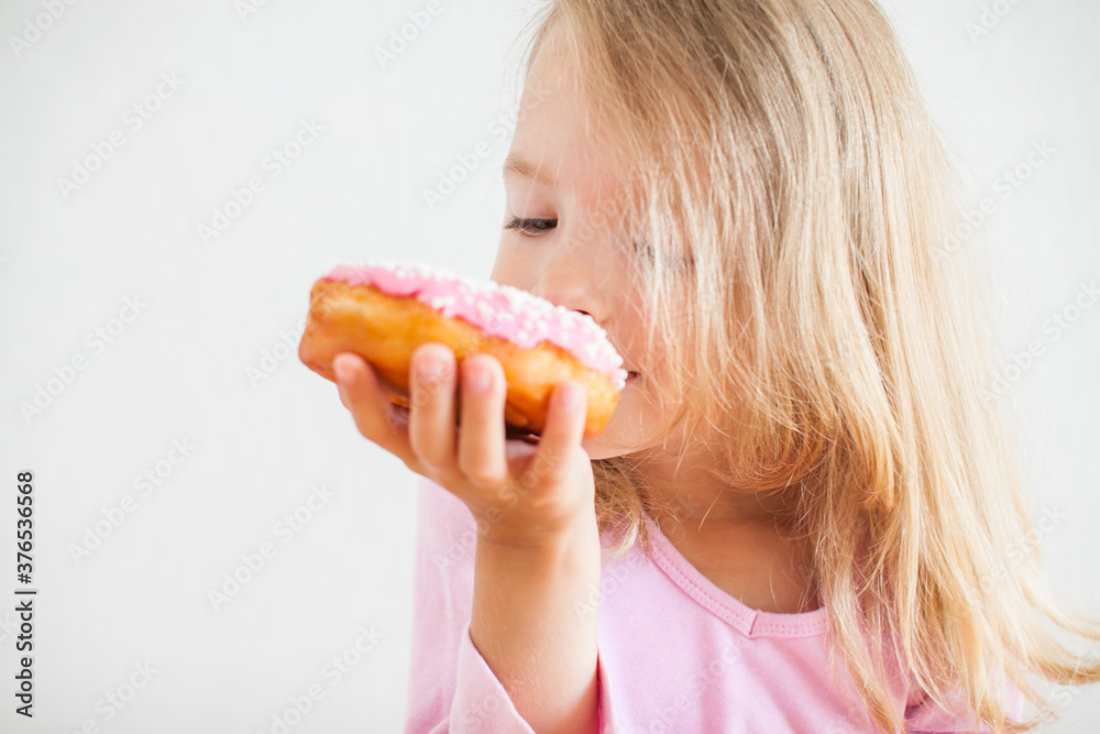 Little happy girl with blond hair playing and tasting donuts with pink icing at hanukkah celebration Little happy girl with blond hair playing and tasting donuts with pink icing at hanukkah celebration