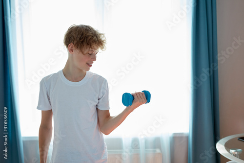 handsome happy teen boy do sport traning at home alone. use dumbbells