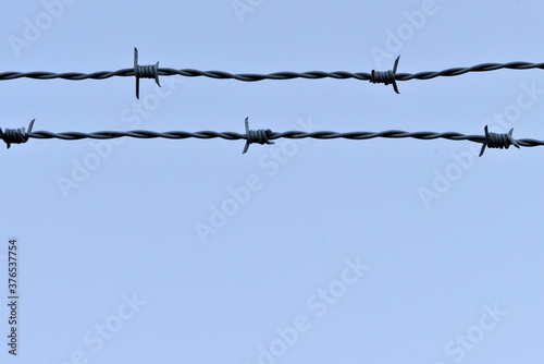Grey barbed wire fence on a blue sky background.