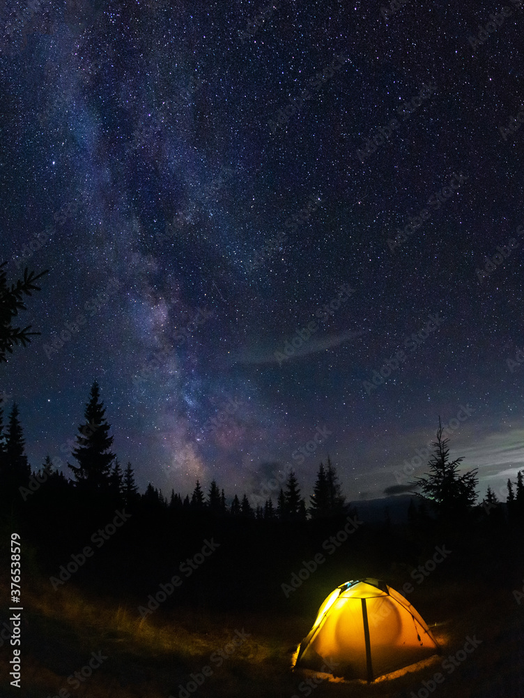 Perseid meteor shower and the Milky Way in the Carpathian Mountains. Evening on a hike. tent glows on a background of night starry sky.