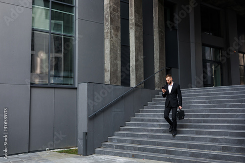 businessman walking from office building and looking at phone ou © Ivan